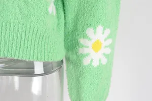Close-up of green knit sweater sleeve with white daisy pattern and soft texture.