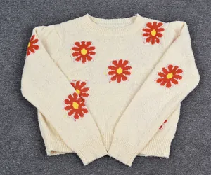 Detailed view of a cream-colored knitted sweater featuring vibrant red daisy floral patterns.