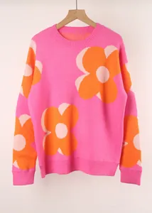 Detail of pink crewneck sweater featuring large orange floral pattern with knit texture.