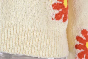 Macro view showing the soft knitted texture and orange daisy pattern of the cream sweater