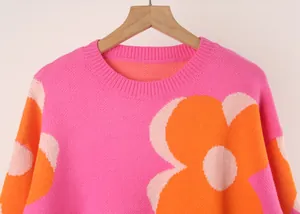 Detailed view of a pink knit sweater featuring a large orange flower and ribbed collar.