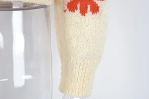Detailed close-up of a cream knit sweater sleeve with an orange daisy floral pattern