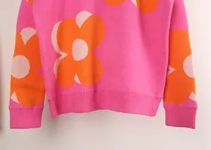 Detail view of pink knitted sweater featuring large orange and white floral print texture.