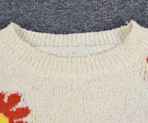 Detailed close-up showing the ribbed crew neckline and soft knit texture of a daisy sweater