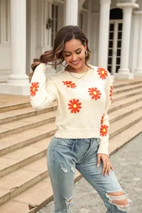 Fashionable cream knit sweater featuring bright daisy floral patterns worn outdoors