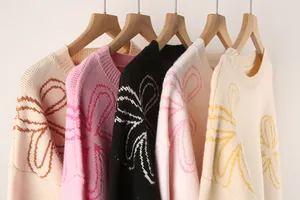 Close-up detail view of colorful knit sweaters with floral patterns on wooden hangers