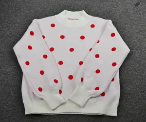 Close-up of white knitted crew neck sweater with vibrant red polka dot pattern
