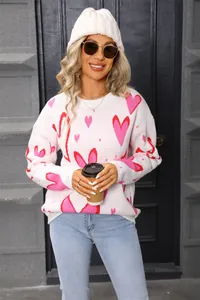 Detailed view of women's loose white knit sweater featuring pink and red heart patterns