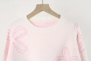 Close-up detail of a soft pink floral knit sweater with a white ribbed crew neckline.