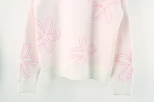 Detailed view of pink long-sleeved knit sweater with white floral patterns and ribbed hem