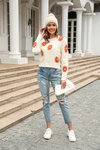 Full body view of a cream knit sweater with orange daisy patterns and ripped jeans