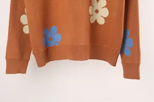 Detail view of orange knit sweater featuring large blue and cream flower patterns.