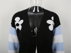 Dettaglio di cardigan in maglia con strisce a contrasto e motivi floreali bianchi.