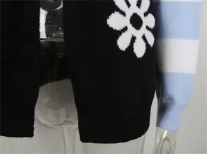 Dettaglio di un cardigan in maglia nera con motivo a fiori e maniche a righe blu e bianche