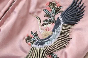 Nahaufnahme der kunstvollen Kranich- und Blumenstickerei auf einer rosa Satin-Bomberjacke.