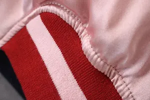 Detailaufnahme des roten Rippbündchens und des seidigen rosa Satinstoffs der Jacke.