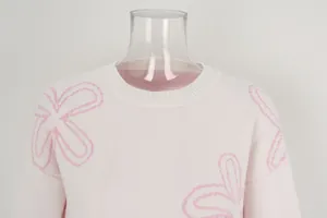 Close-up view of pink round neck sweater with white ribbed collar and floral patterns