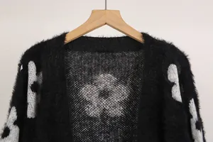 Primer plano de cárdigan de punto negro con textura y motivos de flores blancas