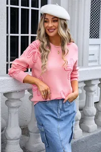 Detail of pink long sleeve crewneck knit sweater with floral pattern on model