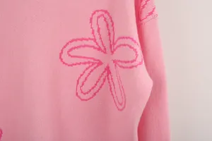 Close-up detail of pink knitted sweater showing stylized floral pattern and texture
