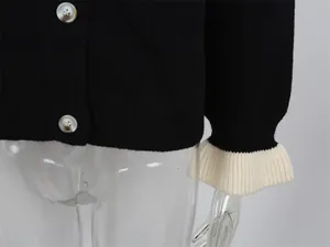 Gros plan d'un cardigan en maille noir avec poignets à volants blancs et boutons