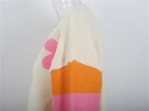Vista dettagliata di un cardigan in maglia con fiore rosa e strisce arancioni e rosa sulla manica.