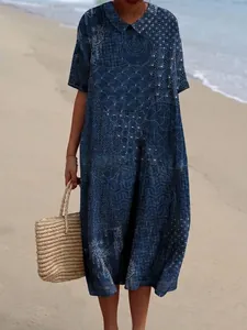 Lange blauwe jurk met print en Peter Pan-kraag in een zonnige strandsetting.