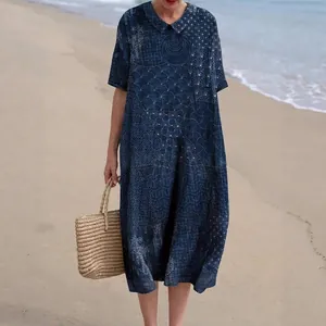 Detailweergave van een blauwe midi-jurk met etnische print en Peter Pan-kraag op strand.