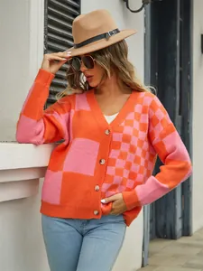 Stylish woman in a pink and orange checkered knit cardigan leaning against a wall