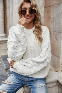 Close-up view of a white knit sweater featuring textured bubble sleeves and ribbed cuffs.