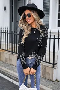 Detailed shot of black knit sweater featuring white floral patterns and round neck.