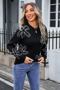 Detailed view of women's black long sleeve knit sweater with white floral outline pattern