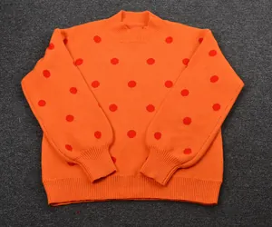 Detail view of an orange knitted pullover sweater featuring a vibrant red polka dot pattern.