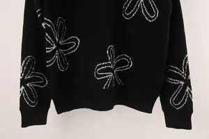 Detail view of black knitted sweater with white floral patterns and ribbed hem and cuffs