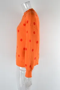 Detailed side view of a cozy orange knitted sweater featuring red polka dots and ribbed cuffs.