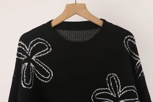 Detailed close-up showing the neckline and white floral pattern on a black knitted sweater
