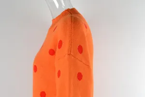 Close-up of vibrant orange knitted sweater featuring bold red polka dot patterns.