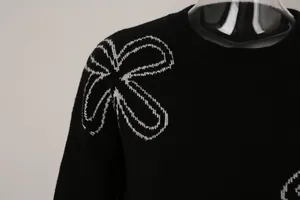 Detailed close-up showing white flower knit pattern on black crew neck sweater shoulder