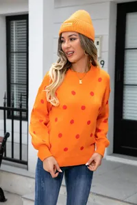 Close-up of vibrant orange polka dot knit sweater worn by model in urban street scene