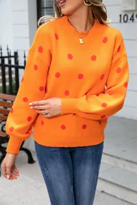 Close-up detail of orange knitted sweater featuring red polka dots and rib-knit cuffs.