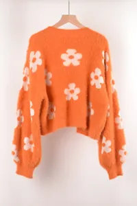 Detalle de la textura suave de un elegante suéter de punto naranja con flores blancas