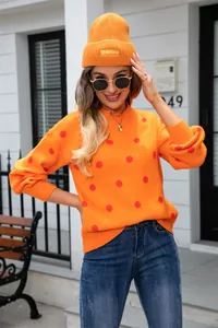 Close-up of bright orange knit sweater featuring red polka dots and matching beanie