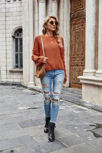 Full body view of a stylish burnt orange knit sweater paired with ripped denim jeans