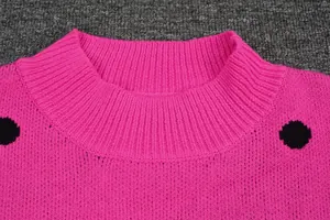 Close-up detail of a pink knitted sweater featuring a ribbed neckline and black polka dots.