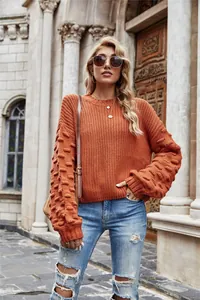 Detail of orange chunky knit sweater with bubble sleeves worn in outdoor setting.