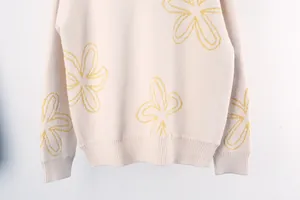 Close-up view of cream knit sweater featuring yellow floral patterns and ribbed hem detail