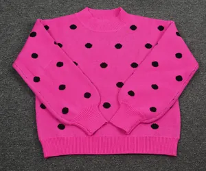 Close-up detail of a bright pink knitted sweater with black polka dots and ribbed cuffs