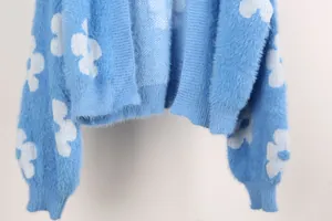 Primer plano de chaqueta de punto azul suave con motivo de flores blancas y textura mullida