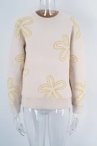 Close-up of beige knit sweater with yellow floral pattern on a transparent mannequin.