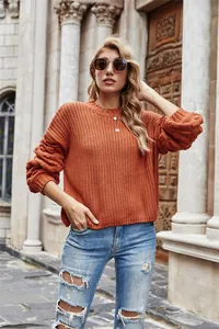 Woman wearing an orange chunky knit lantern sleeve sweater in a city street setting